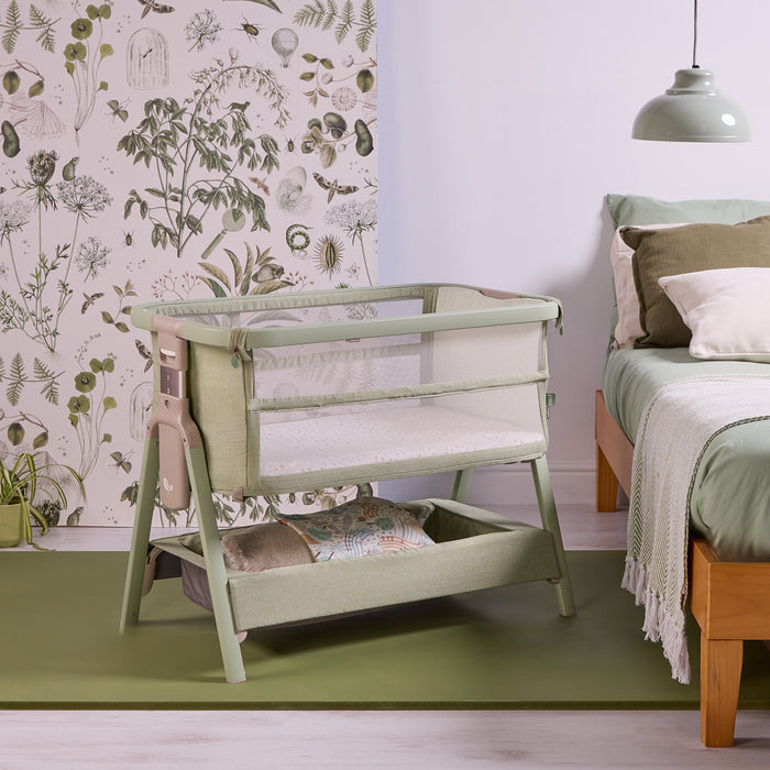 angled view of the CoZee Zen bedside crib in eucalyptus, highlighting its sturdy frame, mesh panels and integrated storage basket.