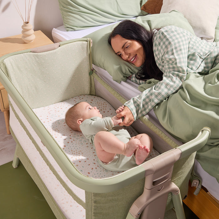 Lifestyle image of a parent and baby interacting beside the bed using the CoZee Zen bedside crib in eucalyptus finish.