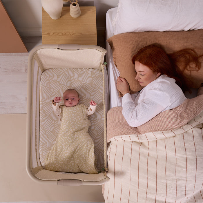 Overhead view of baby sleeping next to parent in the CoZee Zen bedside crib, illustrating closeness, comfort and safe sleep design.