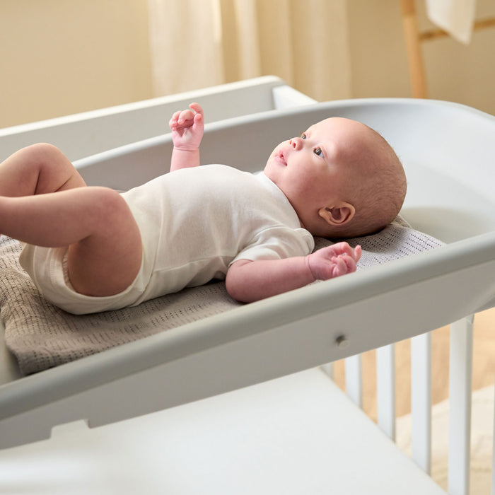 Close-up of baby resting on the Cushi baby changing mat in cloud grey, highlighting comfortable
support and secure raised edging