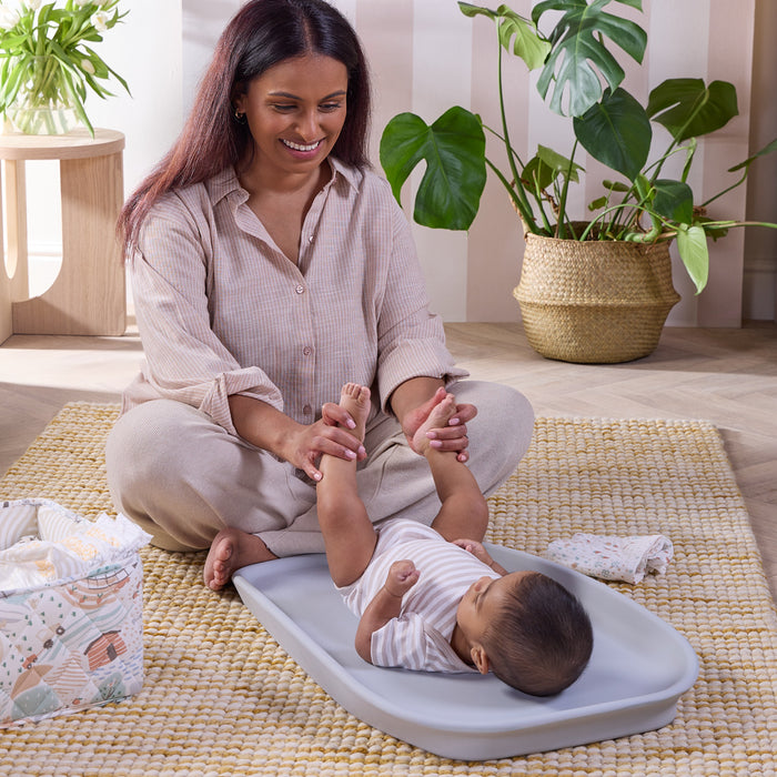 Mum changing baby on the Cushi mini changing mat in cloud, showing supportive design for comfortable, everyday nappy changes