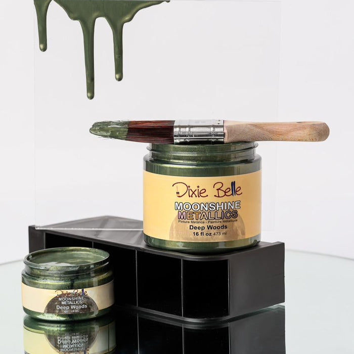 Jars of 'Dixie Belle Moonshine Metallics' paint with a brush on a glass surface.