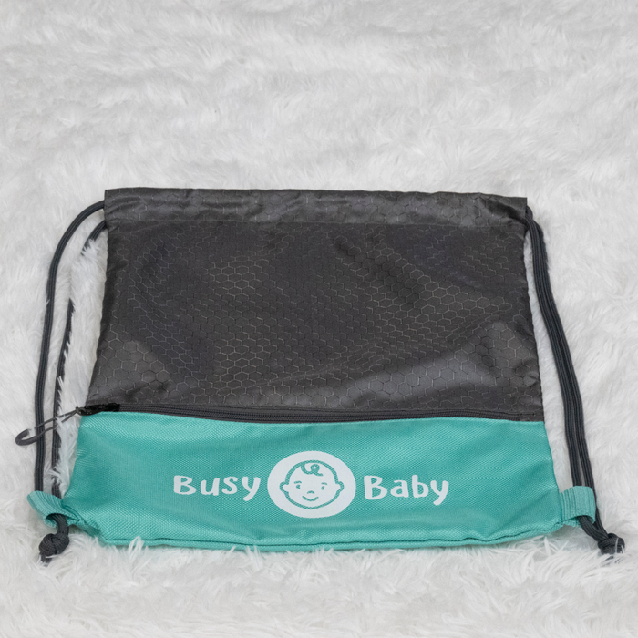 A black and teal Busy Baby Drawstring Backpack with the words "Busy Baby" and a baby face logo printed on the teal section lies on a fluffy white carpet, showcasing high-quality Busy Baby gear.