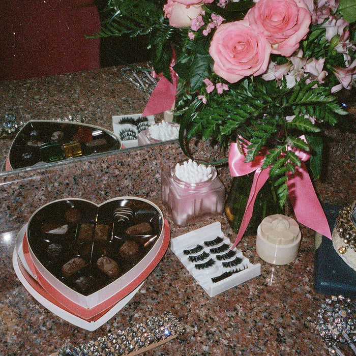 Close-up of a heart-shaped chocolate box a bouquet of pink roses false eyelashes and a crown on a bust