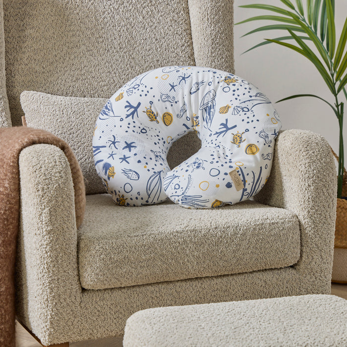 Our Planet white feeding pillow with blue and yellow ocean-inspired patterns on a beige nursing chair