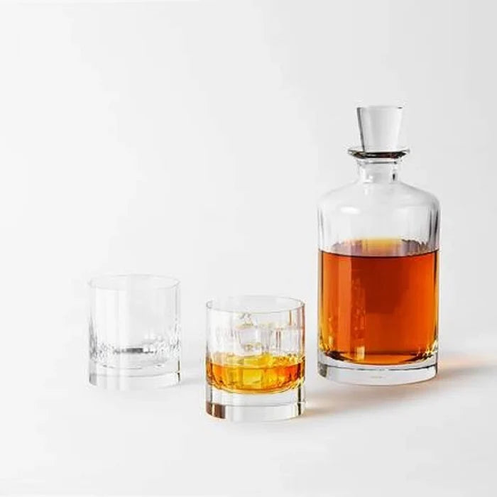 The Richard Brendon Fluted Shot Glass Set of 2 stands beside a mouth-blown glass decanter filled with amber liquor—an elegant barware addition—displayed on a white surface against a plain white background.