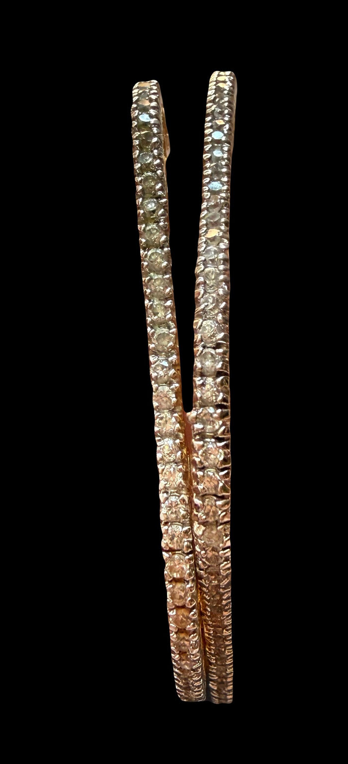 A pair of gold-toned bangles decorated with rows of clear pavé-set stones, shown against a solid black background.