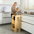 Mum supervises toddler standing safely in the Helping Hands Montessori learning tower in natural finish, perfect for interactive family activities