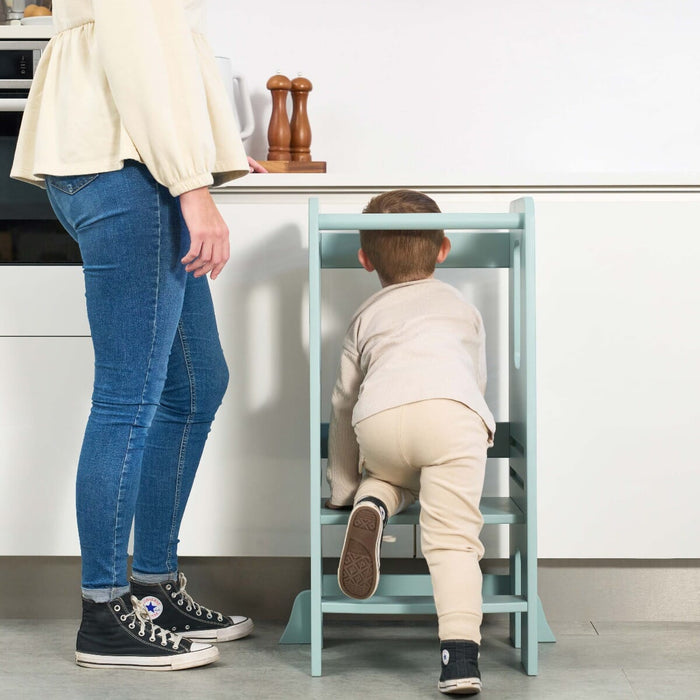 Toddler climbing the Helping Hands Montessori learning tower in ocean stone, showing secure steps and sturdy frame for safe kitchen use