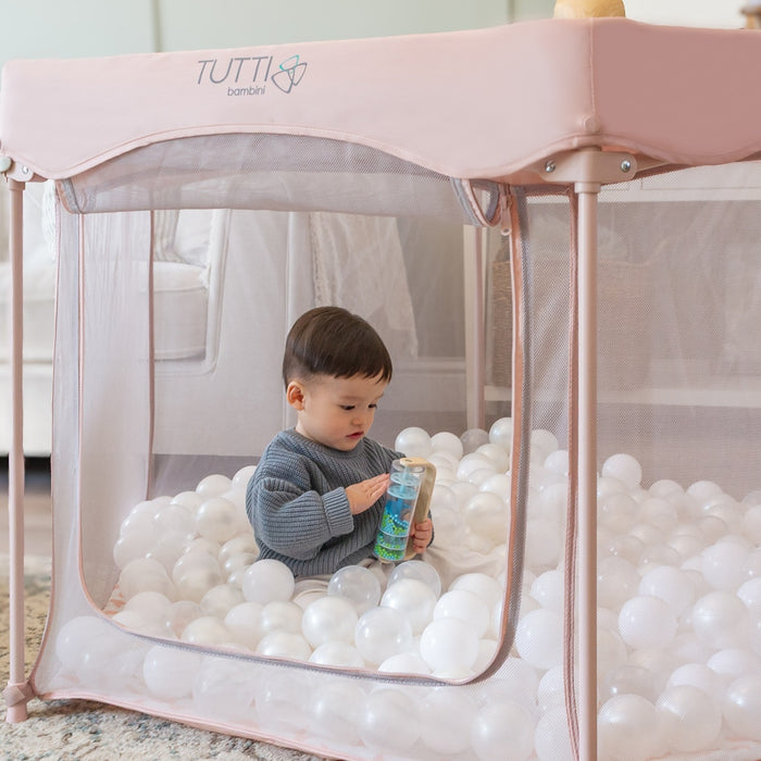 Toddler playing with toys inside the Hexa Playpen in Gumdrop Terrazzo, filled with white play balls and soft padded flooring