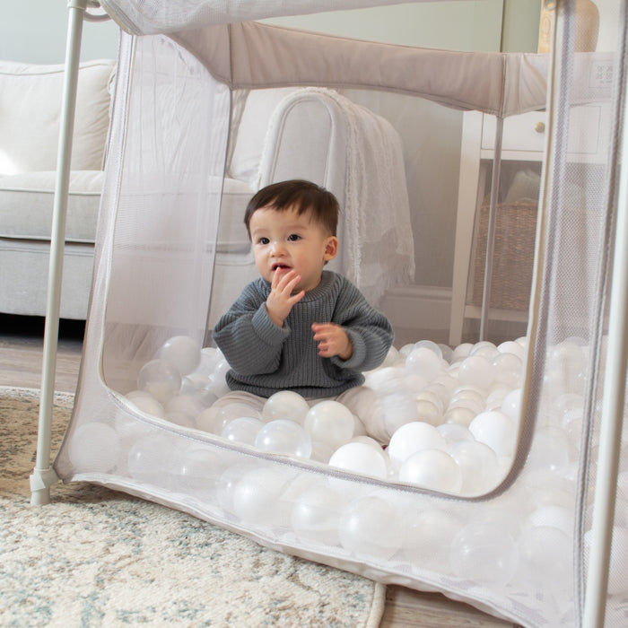 Child playing inside the Hexa Playpen in mushroom terrazzo, filled with soft white play balls and zip-down side open for easy access