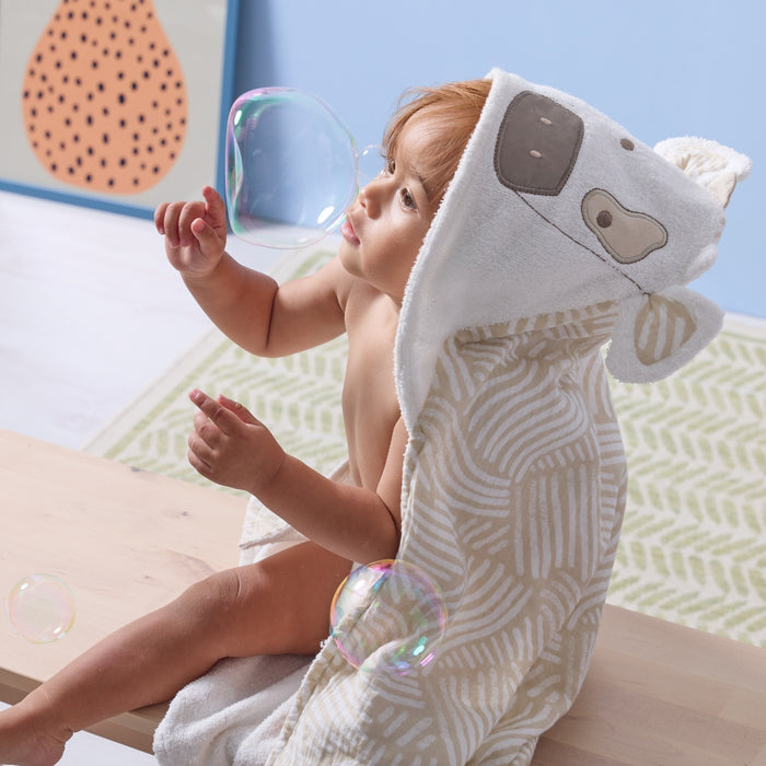 Side view of toddler wearing Clemi the Cow hooded towel, reaching for bubbles, showing detailed embroidered face