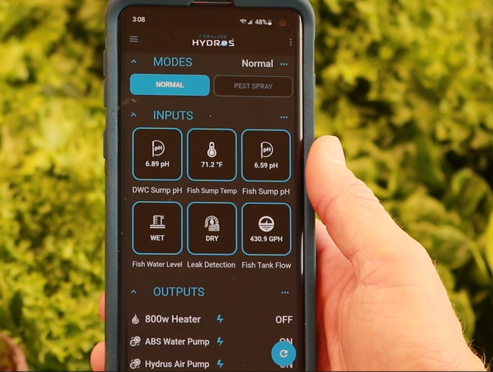 A person holding up a smartphone with a green screen, utilizing TAS HYDROS Control X3 Controllers for controlling pumps and monitoring sensors.