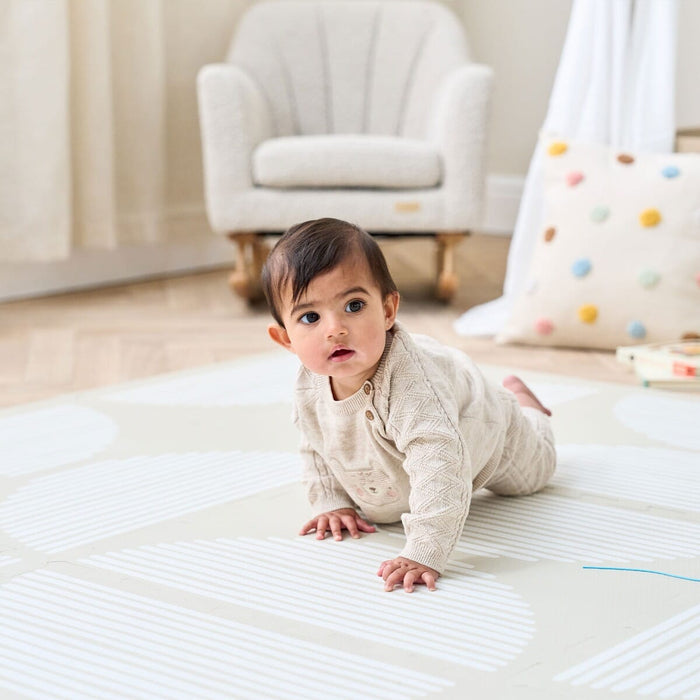 Baby crawling on the Orbital Oatmeal infinity playmat on a neutral bedroom with a rocking chair on the background.