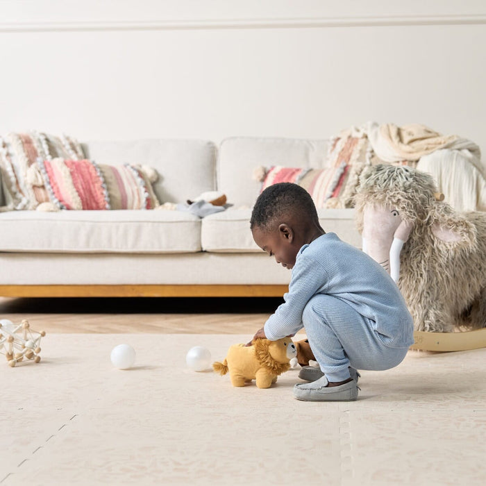 Child playing on Bedouin Sand Playmat, set in a neutral living room with seating furniture and a rocking animal toy.