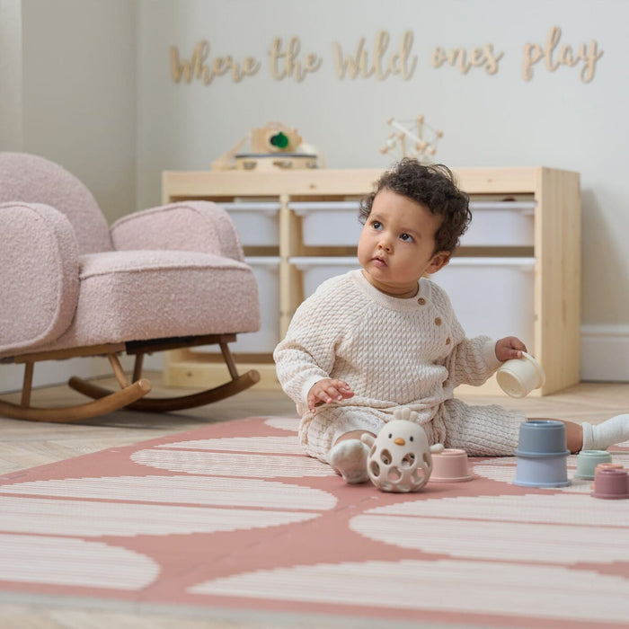 A child playing on the Orbital Nutmeg Baby Infinity Playmat on a playroom with a mini rocking chair.