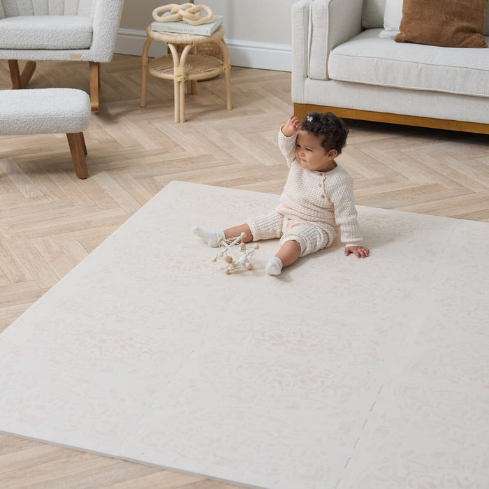 Baby on Bedouin Sand Playmat, set in a neutral living room with seating furniture.