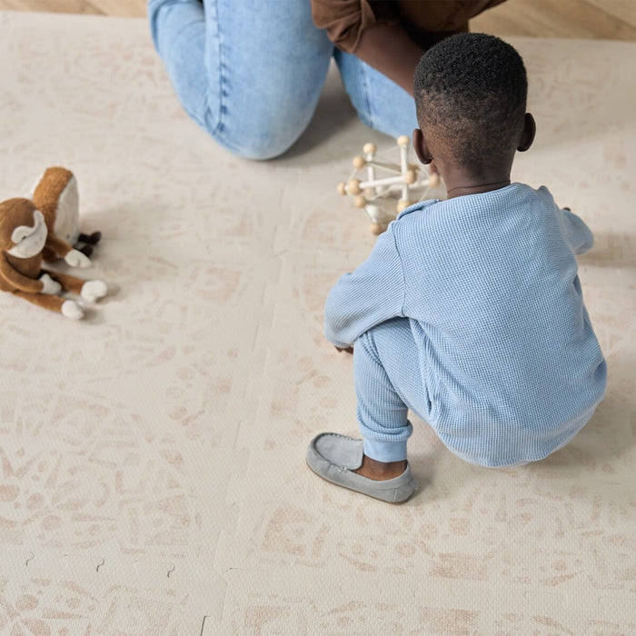 A child dresses in a blue pyjamas playing on the Bedouin Sand playmat.