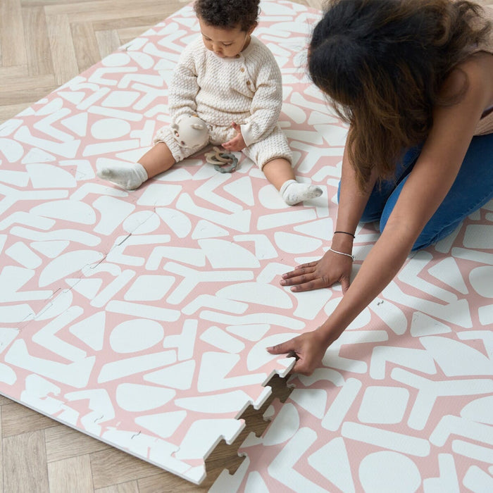 A child and a woman connecting the pieces of the Oddity Blush infinity playmat.