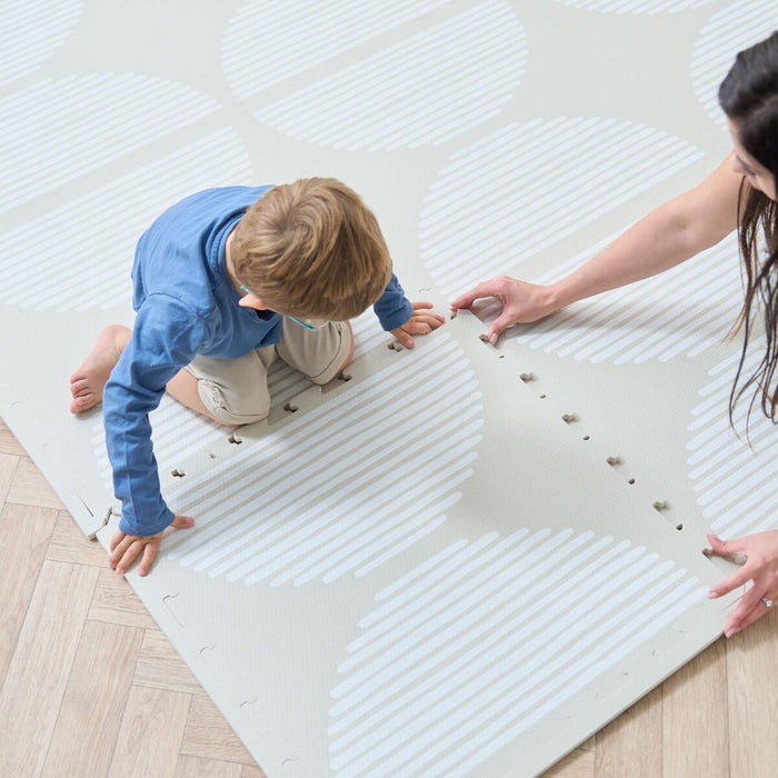 A child and a woman connecting the pieces of the Orbital oatmeal infinity playmat.