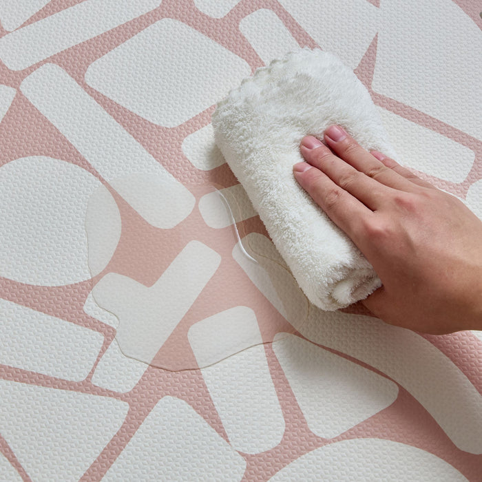Hand wiping water off the pink and white Oddity Infinity Playmat, highlighting its easy-to-clean surface.