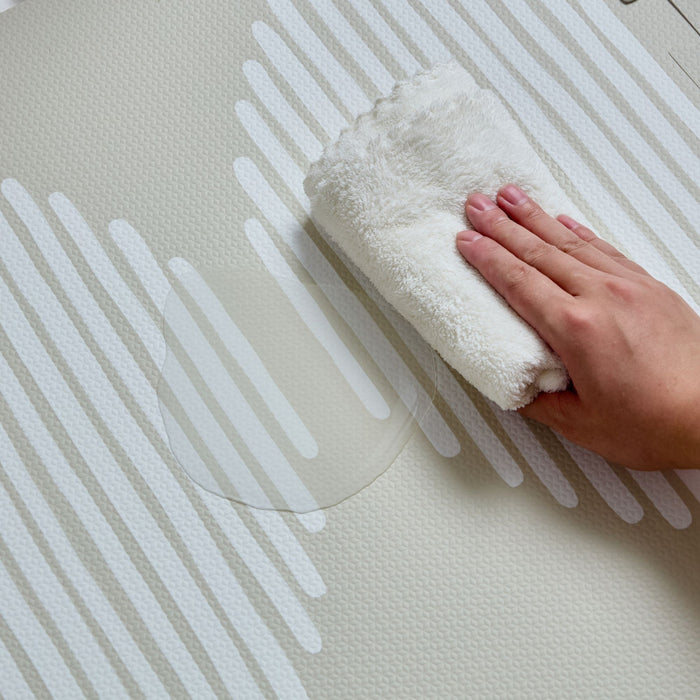 Hand wiping water off the oatmeal and white Oddity Infinity Playmat, highlighting its easy-to-clean surface.