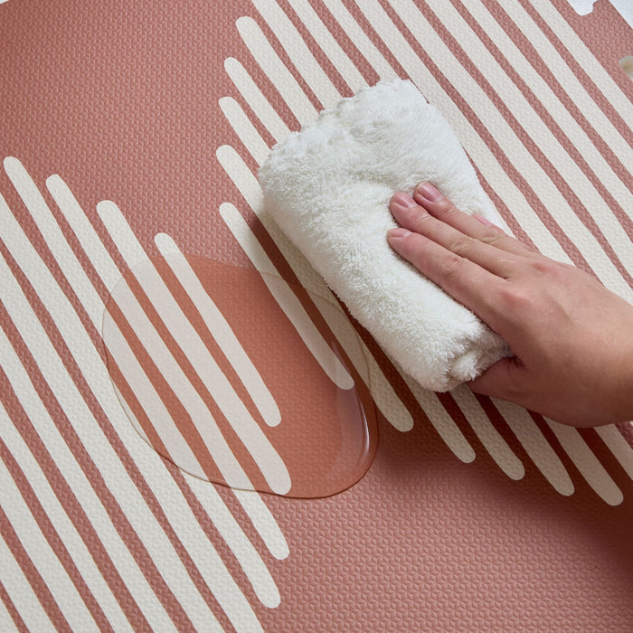 Hand wiping water off the pink and white Orbital Infinity Playmat, highlighting its easy-to-clean surface.