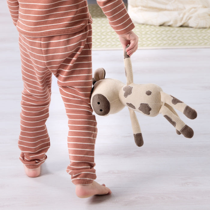 Child wearing orange and white striped pyjamas holding a Clemi cow knitted toy.