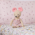 Margot Mouse knitted toy sitting on a floral-patterned bedspread with a pink background.