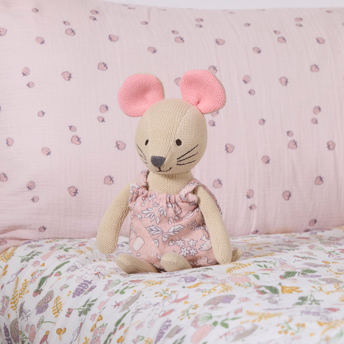 Margot Mouse knitted toy sitting on a floral-patterned bedspread with a pink background.