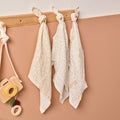 Three baby muslins hanging on a wooden rack against a beige wall.