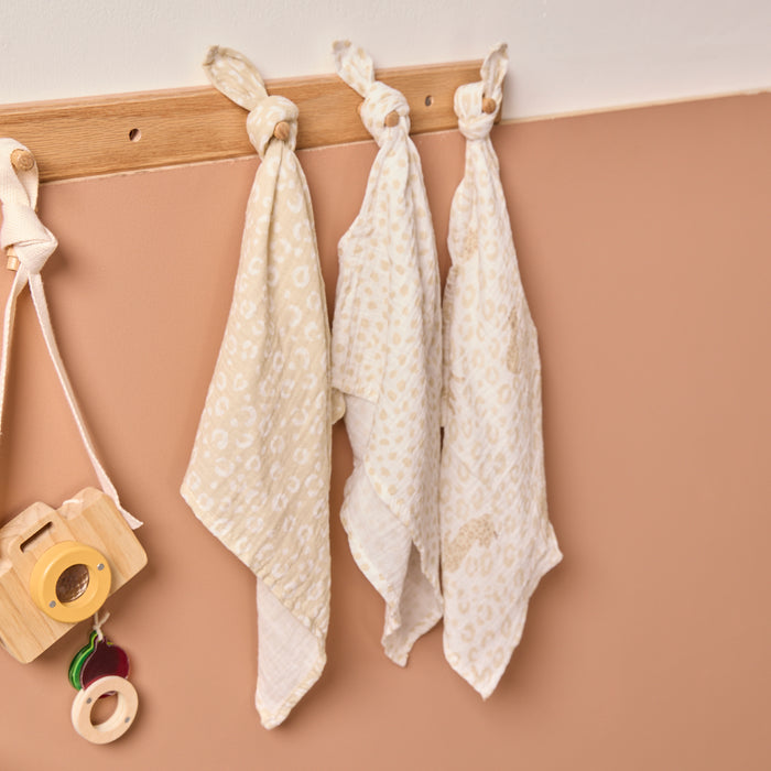 Three baby muslins hanging on a wooden rack against a beige wall.