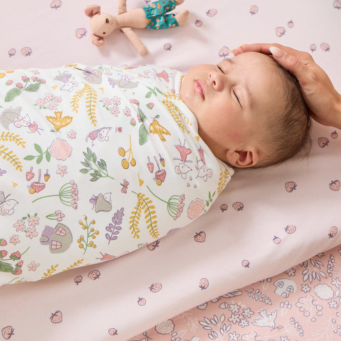 Baby peacefully sleeping swaddled in Tiny Tails muslin with woodland print
