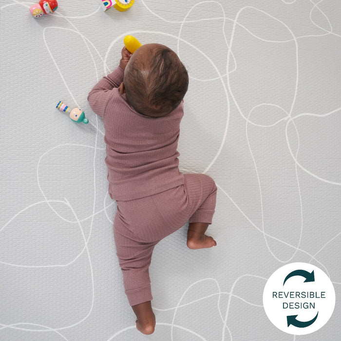 Baby crawls on the mat’s grey reversible side, featuring soft contour lines and cushioned support for comfortable tummy-time play