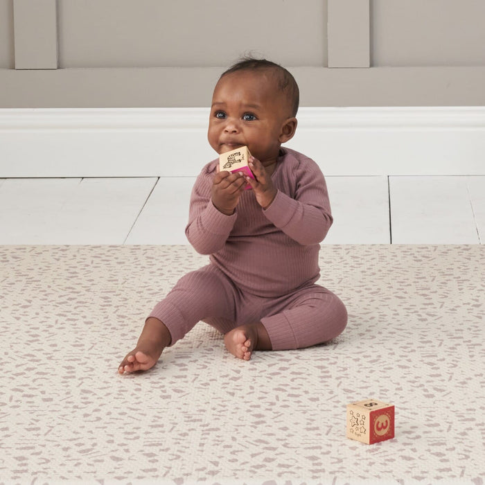 Baby sits on the Bubble Terrazzo play mat holding a wooden block, with soft neutral pattern providing a calm, cushioned play surface