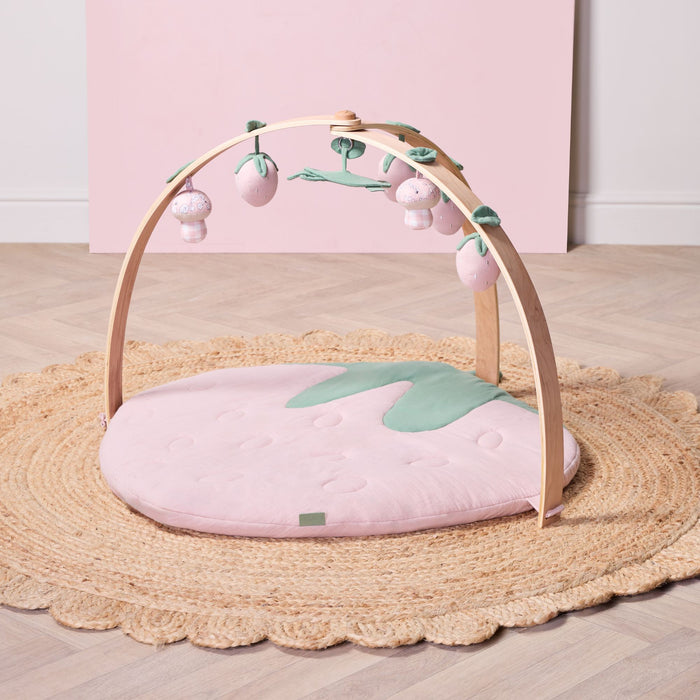 Strawberry muslin baby playmat with wooden playgym arch and soft hanging toys styled on woven rug.