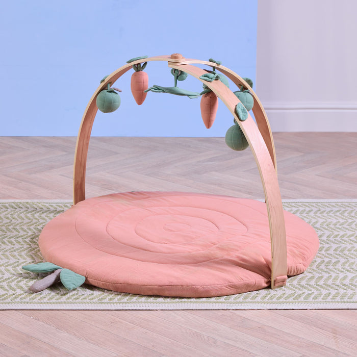 Terracotta muslin baby playmat with wooden playgym arch and soft hanging toys styled in nursery setting.
