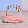 Terracotta muslin baby playmat with wooden playgym arch and soft hanging toys styled in nursery setting.