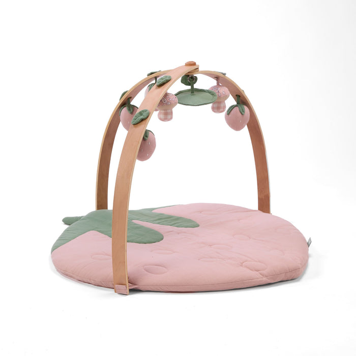 Strawberry-shaped muslin padded playmat with wooden arch playgym and hanging strawberry and mushroom toys.