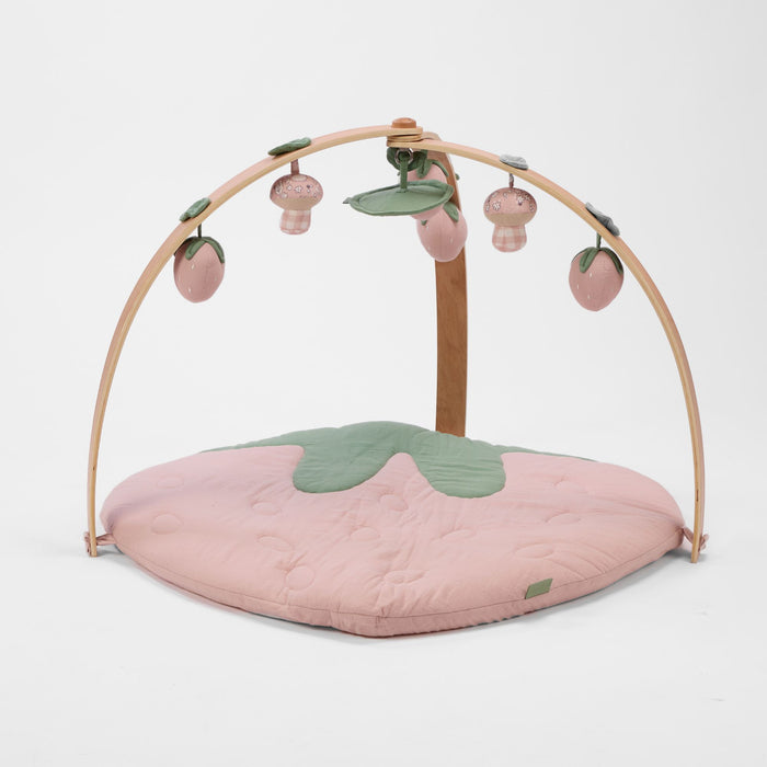 Strawberry-shaped muslin padded playmat with wooden arch playgym and hanging strawberry and mushroom toys.