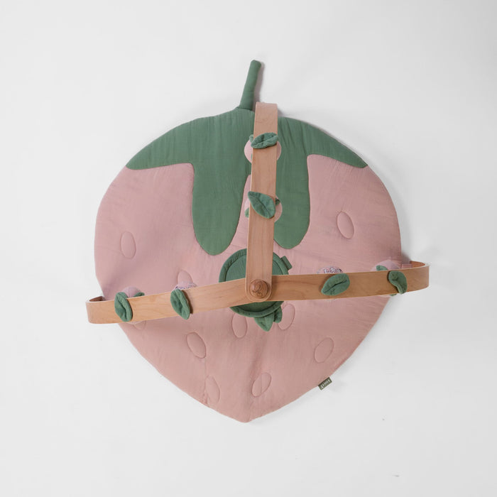 Top-down view of strawberry-shaped padded muslin playmat with wooden playgym arch and leaf details.