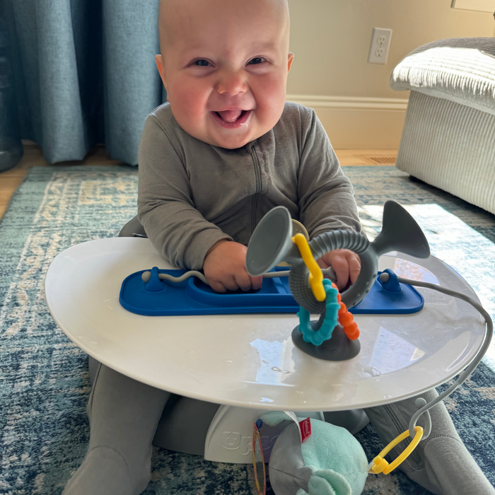 baby in travel seat with blue busy baby mini mat suctioned to tray and toys attached to tethers