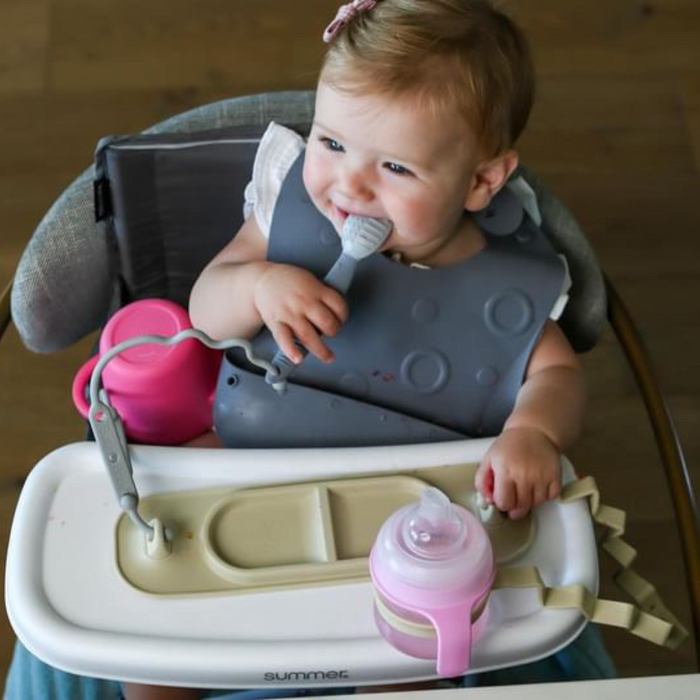 baby sitting in travel high chair chewing on spoon connected to busy baby mini suction placemat with tethers