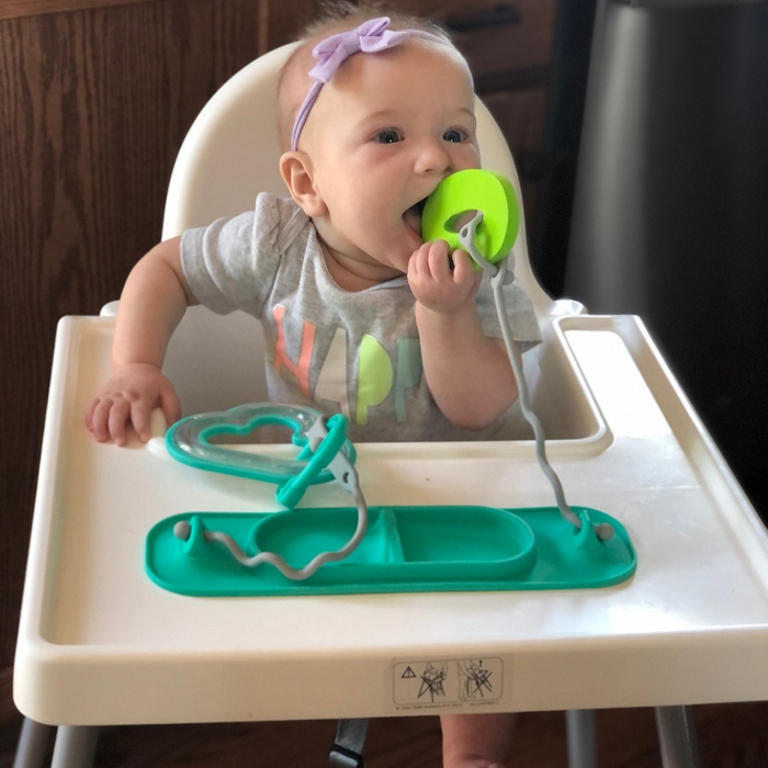 baby sitting in highchair chewing on toy attached with tethers to busy baby suction mini placemat