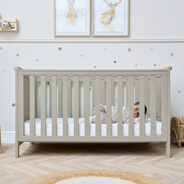 Baby lying inside a Misha Cot Bed in Mushroom in a neutral-colour nursery.