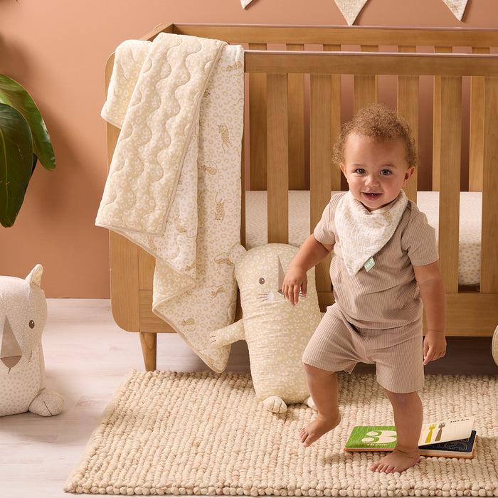 Baby standing in a cot bed with toys and a blanket from the Love Cats collection in a nursery setting