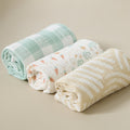 Three rolled Good Life muslin cloths in sage gingham, carrot print and neutral stripe, styled to highlight soft, breathable cotton texture.