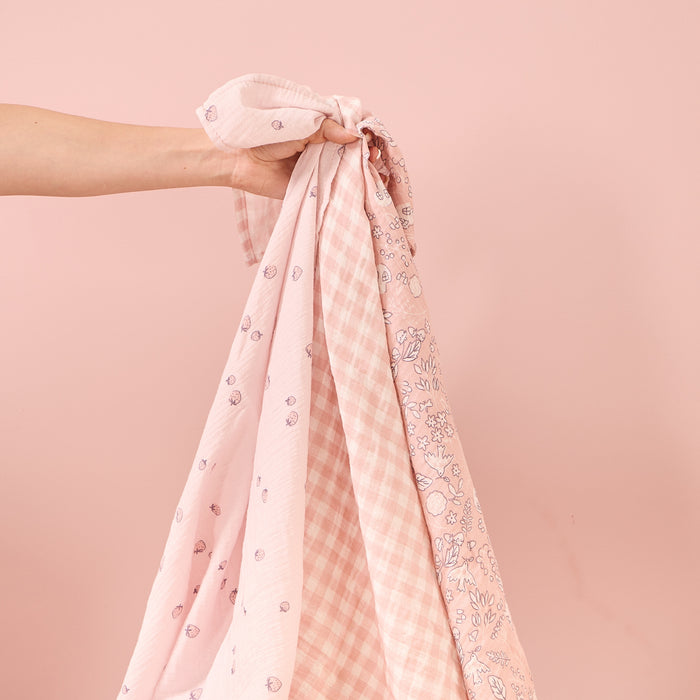 tiny tails muslin sqaures being held up to showcase the three contrasting soft pink floral patterns.