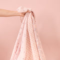 tiny tails muslin sqaures being held up to showcase the three contrasting soft pink floral patterns.