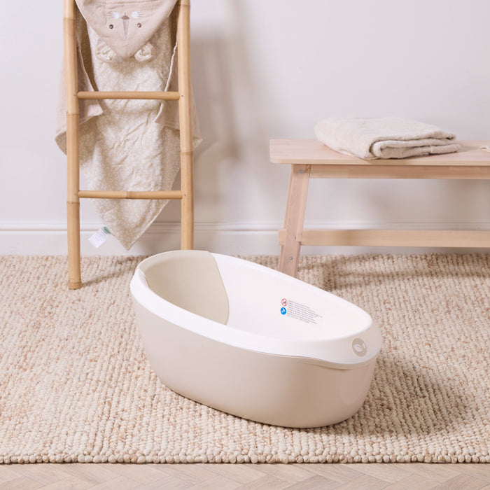 Nati Baby Bath in dune placed on a textured rug beside natural wood furniture, creating a calm and practical bath space.